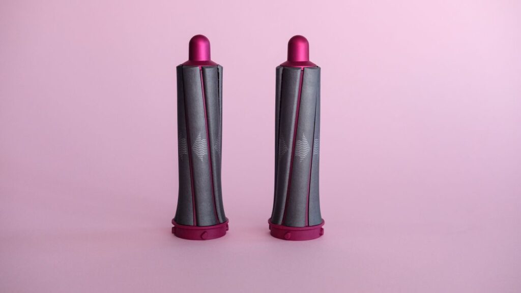 Dyson Stylingaufsatz in Pink und Grau auf rosa Hintergrund, geeignet fuer Praezisionsstyling bei Haarverlaengerung