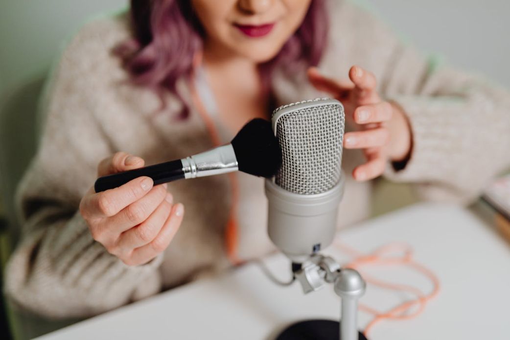Frau hält einen Make-up-Pinsel vor ein Mikrofon und erzeugt ASMR-Geräusche in einem heimischen Setup.