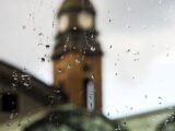 Blick durch regennasses Fenster auf den Hamburger Michel – typisches Wetter, das eine Terrassenüberdachung in Hamburg sinnvoll macht